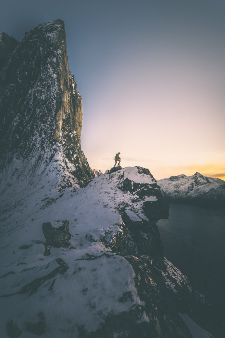 Un homme surplombe une falaise en Norvège avec de la neige tout autours de lui.