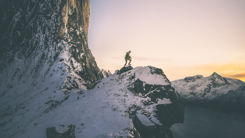 Un homme surplombe une falaise en Norvège avec de la neige tout autours de lui.