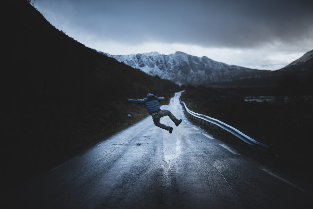 Un homme saute sur une route de norvège avec une montagne au loin